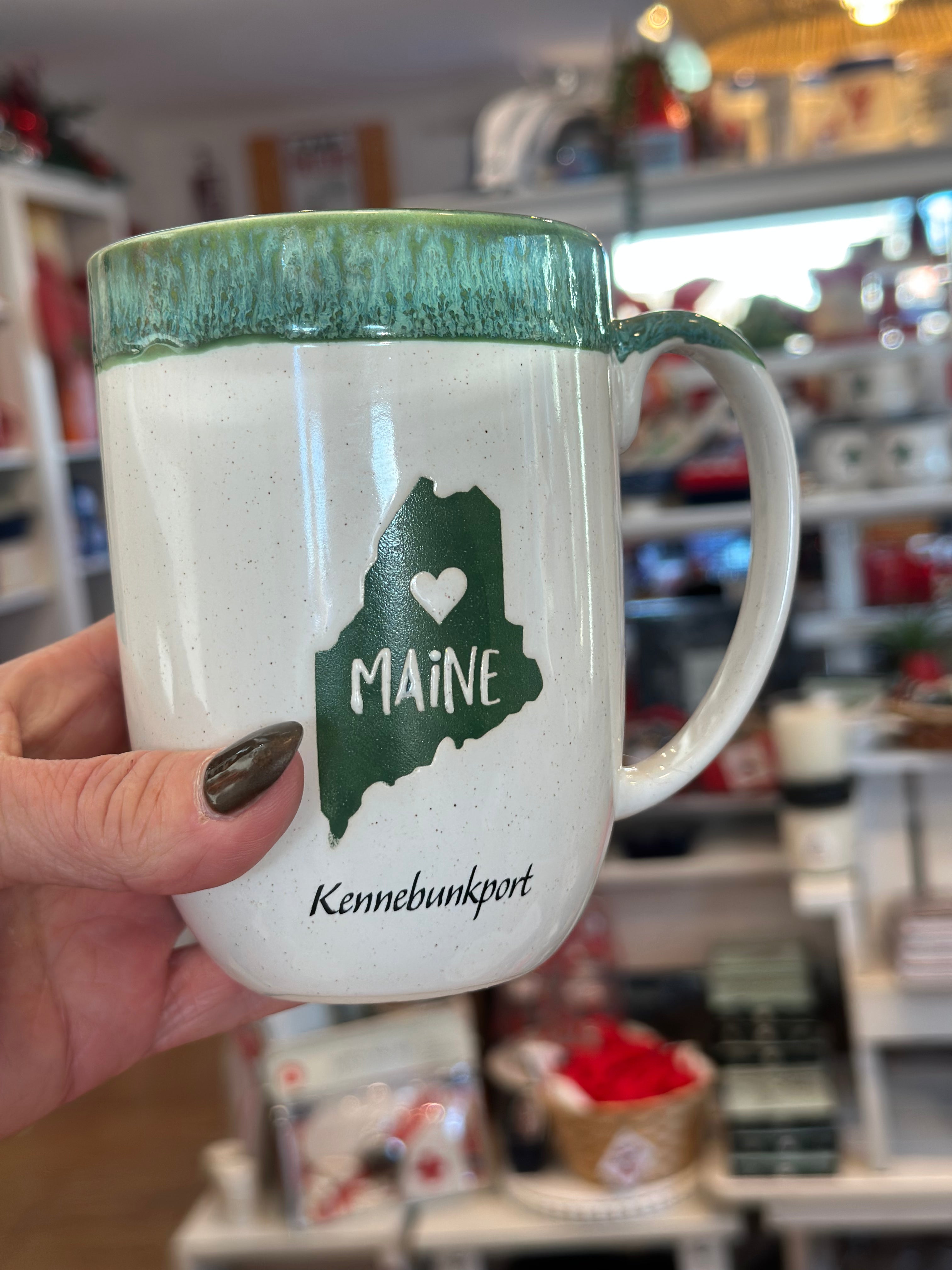 Mug with 'Maine' and 'Kennebunkport' design held by a person in a store setting.