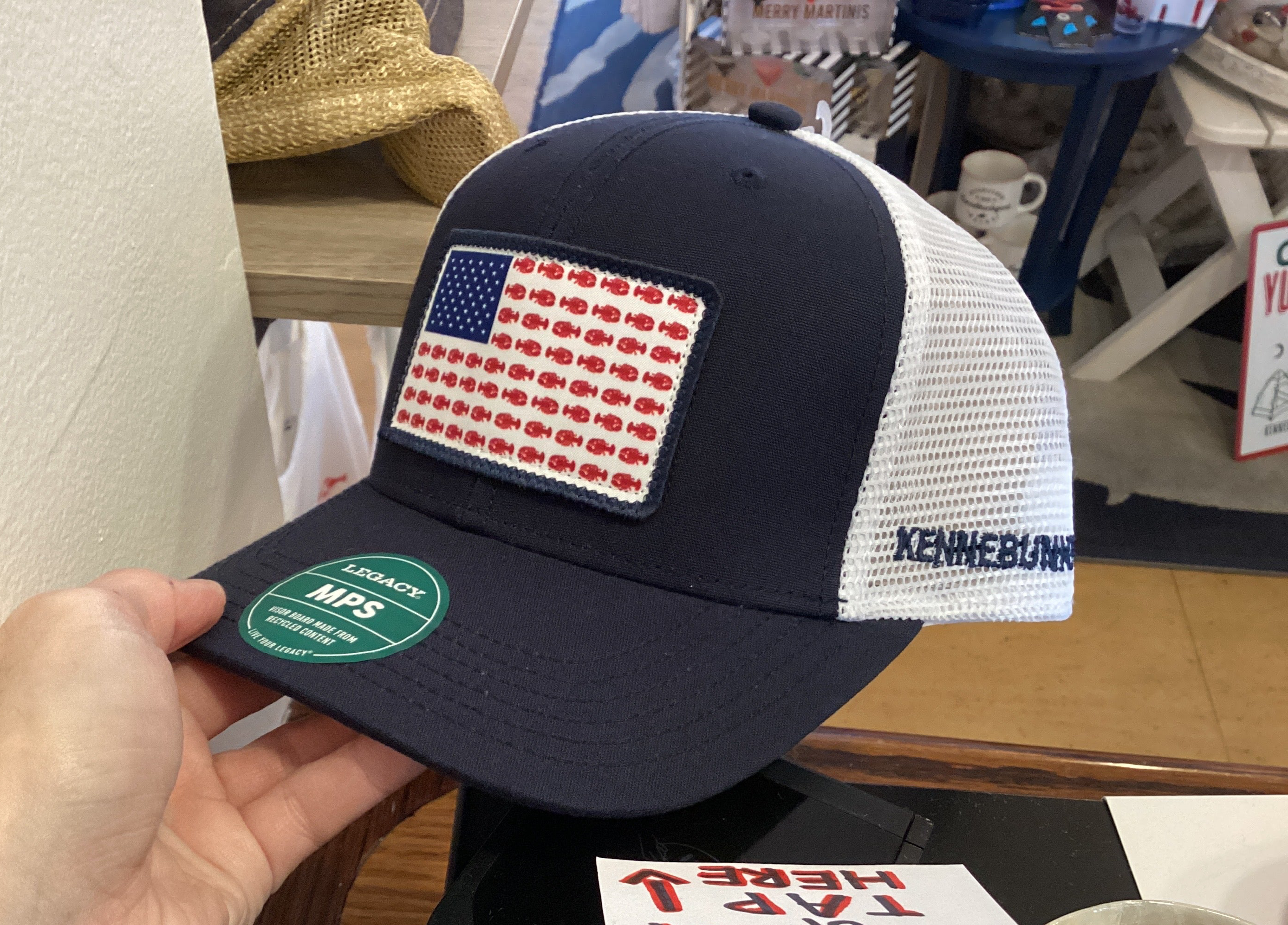 Navy blue cap with American flag patch held by a hand in an indoor setting.