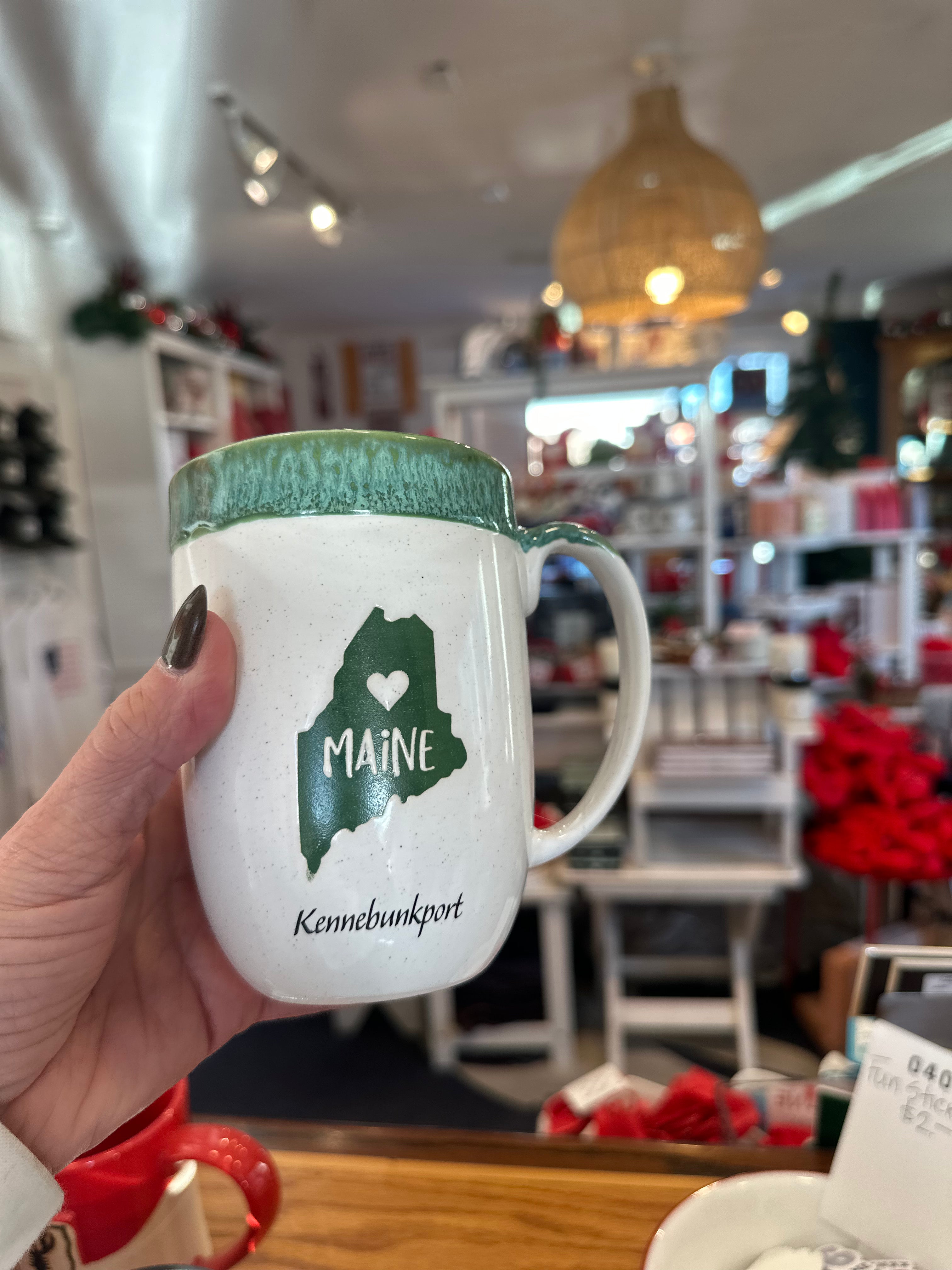 Mug with 'Maine' and 'Kennebunkport' design held in a hand inside a store.